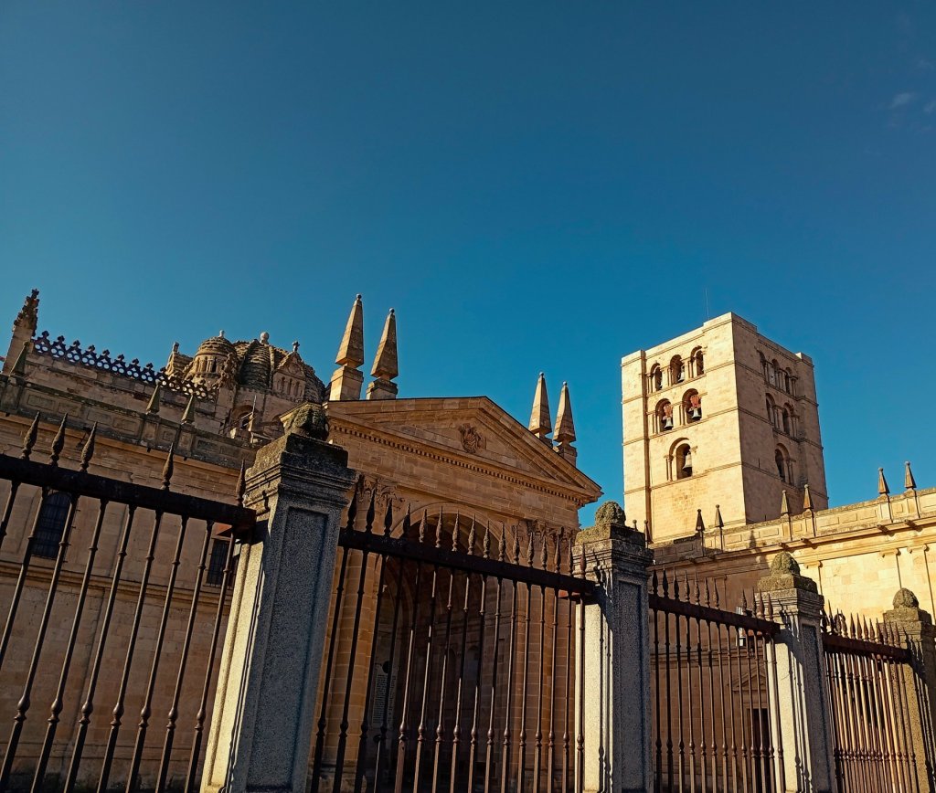 Torre románica y cimborrio de la catedral de Zamora tras la verja, contra un cielo azul.