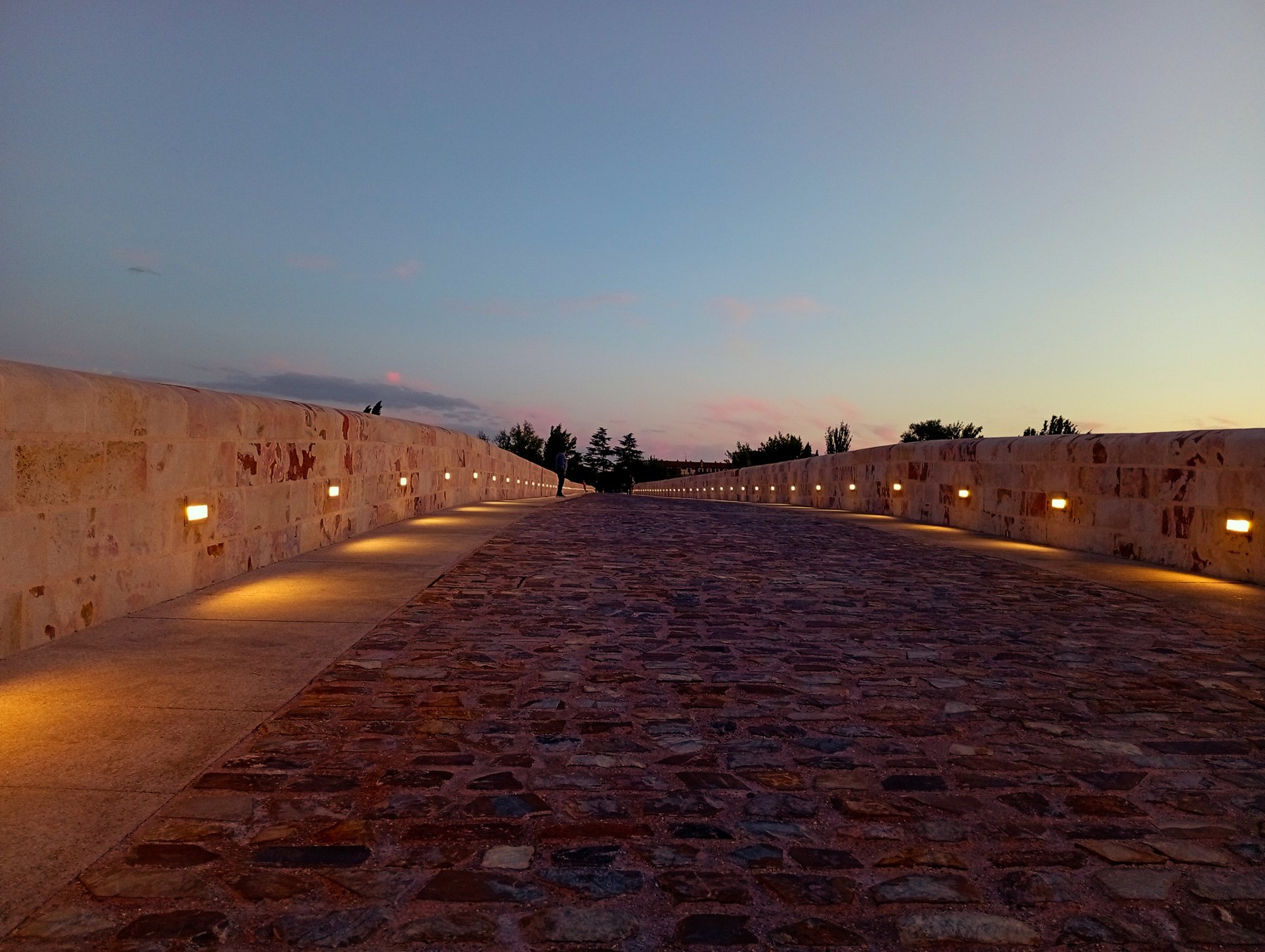 Calzada empedrada del Puente de Piedra de Zamora al anochecer, con luces bajas a ras del pretil.