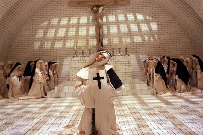 Fotograma de Los demonios, de Ken Russell (1971): una monja arrodillada ante el altar, bajo un gran crucifijo, rodeada por el resto de la comunidad.